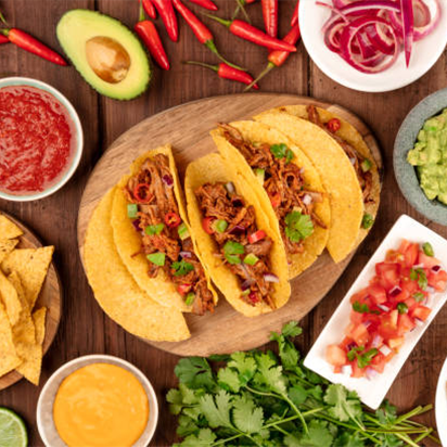 Three tacos with shredded meat and vegetables on a wooden plate