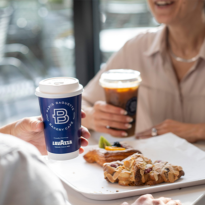 Two people enjoying coffee and pastries at a café, with one holding a cup and the other an iced coffee