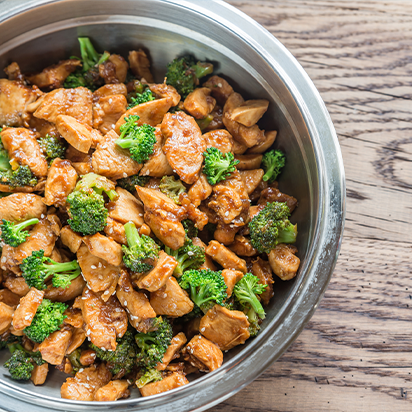 Stir-fried chicken with broccoli served in a stainless steel bowl on a wooden table