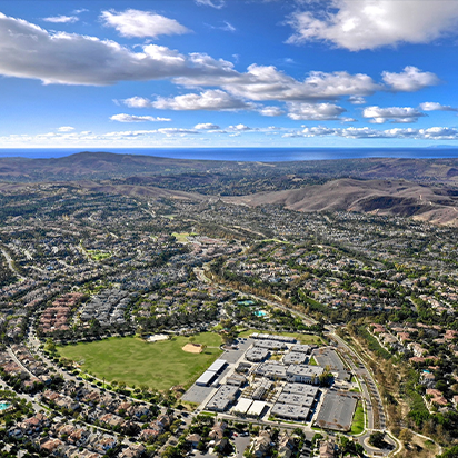 Aerial view of a suburban area with houses, roads, a school building, a green park, and mountains