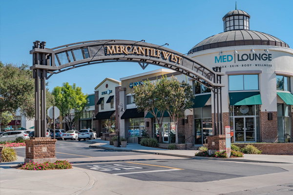 Entrance archway labeled 'Mercantile West' leading into a shopping center with stores and a building featuring a sign for Med Lounge